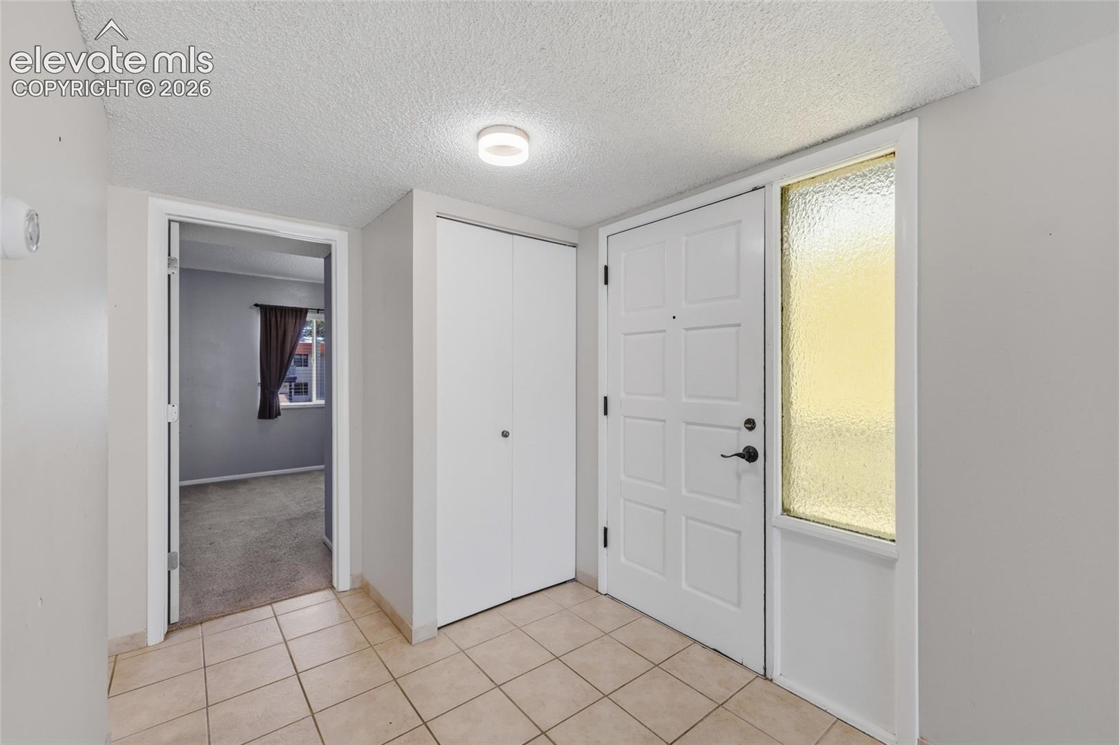 Entryway featuring square tile flooring, a paneled door with a textured glass sidelight, built-in dual-panel closet, and flush-mount lighting