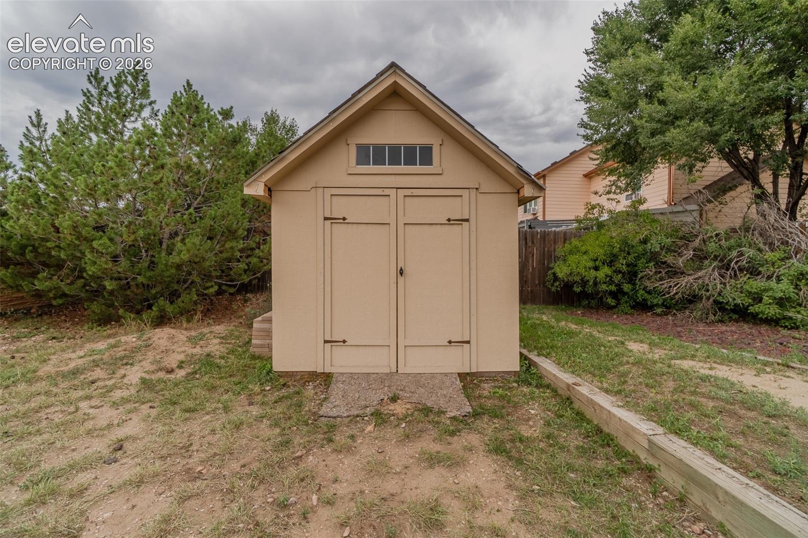 Gable-roof storage shed featuring louvered transom windows and hinged double doors with dark-toned hardware