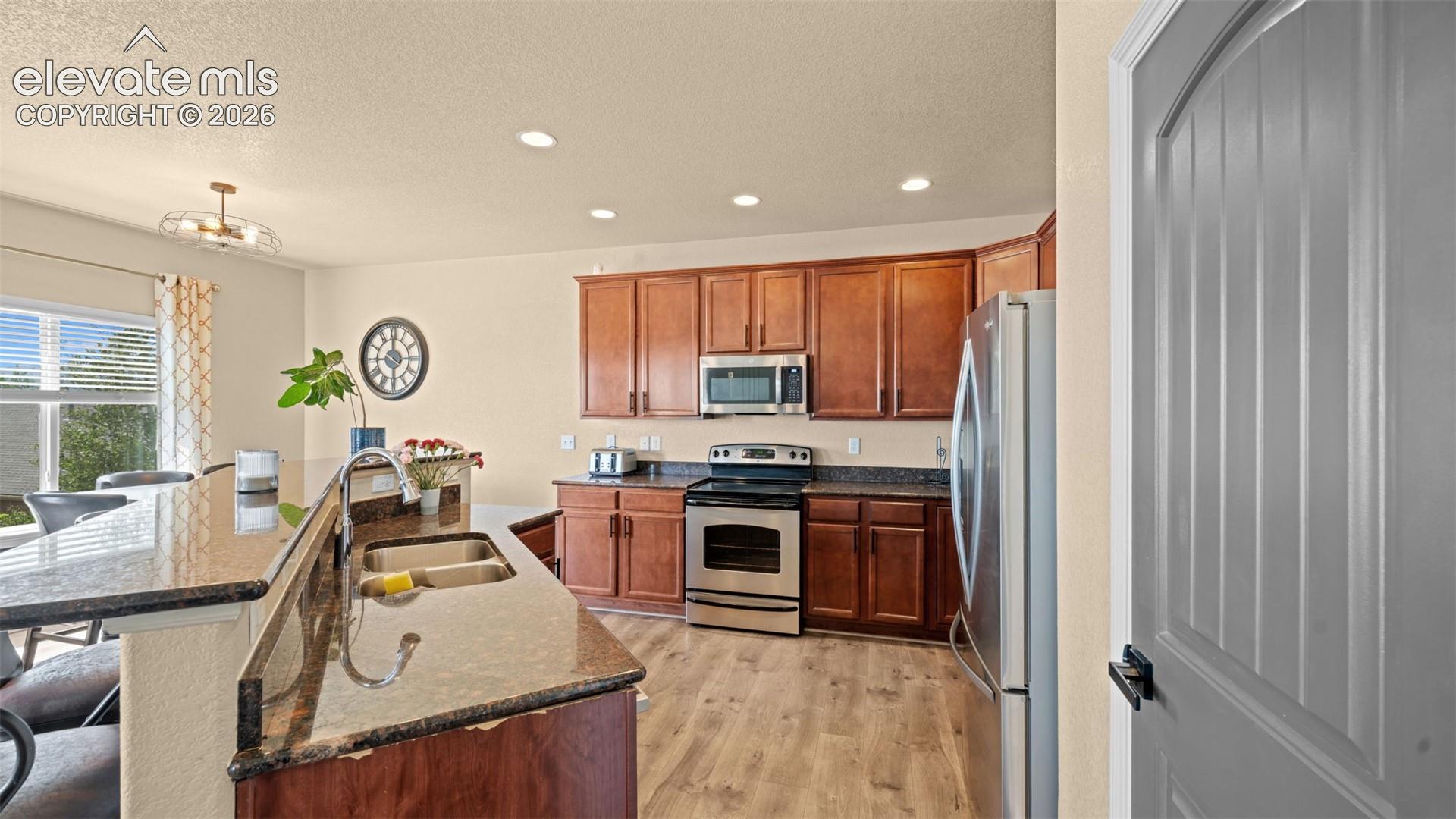Kitchen featuring a large island with sink, wood-finish flooring, stainless steel appliances, recessed lighting, and a window with horizontal blinds