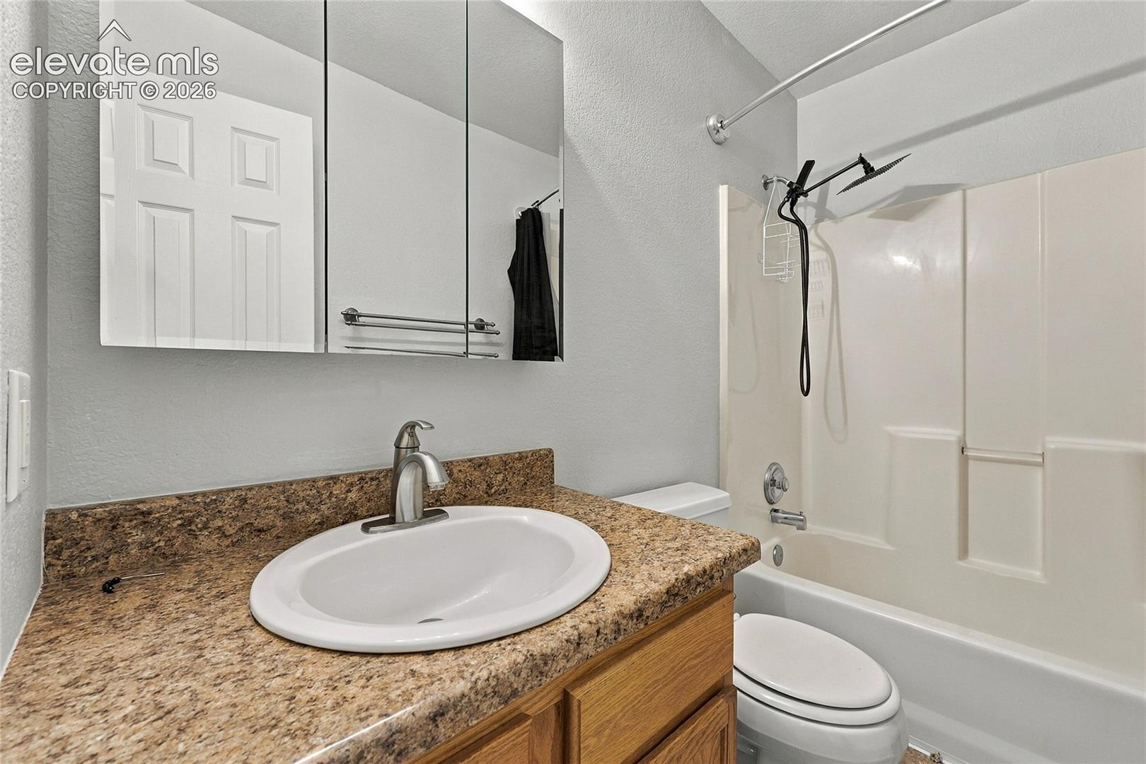 Bathroom featuring a stone-composite countertop, undermount oval sink, wood-finish cabinetry, tri-fold medicine cabinet, and a shower-tub combination with a matte black shower fixture