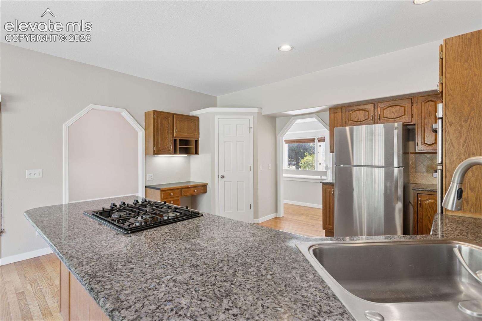 Kitchen featuring a gas cooktop, stainless steel refrigerator, granite-style countertops, and wood-finish cabinetry