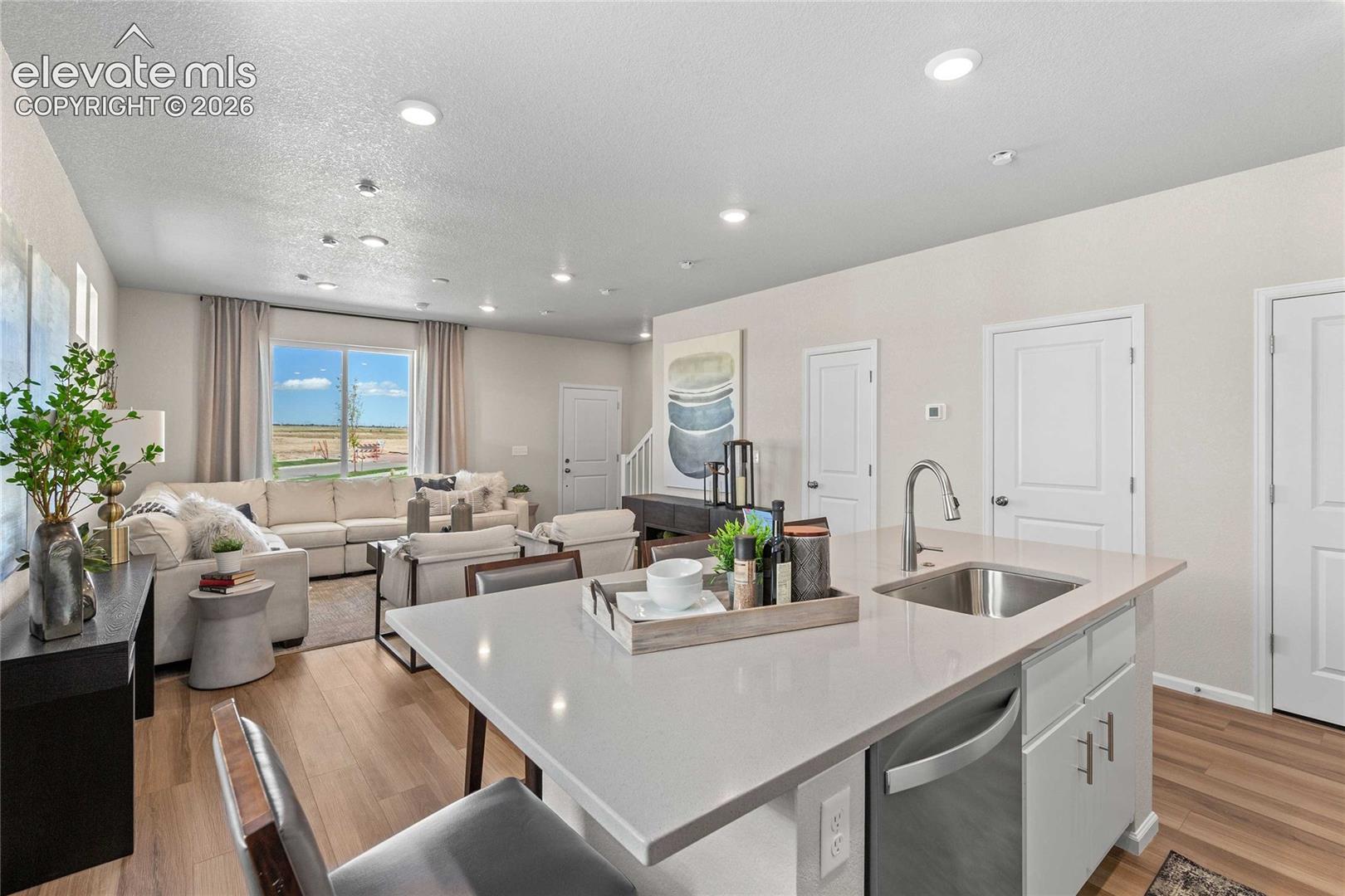 Open-concept living space featuring wood-finish flooring, recessed lighting, and a kitchen island with an integrated sink and stainless steel dishwasher
*photos of a model home*