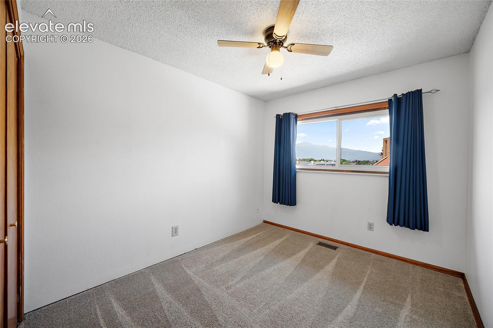 Bright room featuring a window with mountain scenery, a ceiling fan, light-colored carpet, and a wood-finish door
