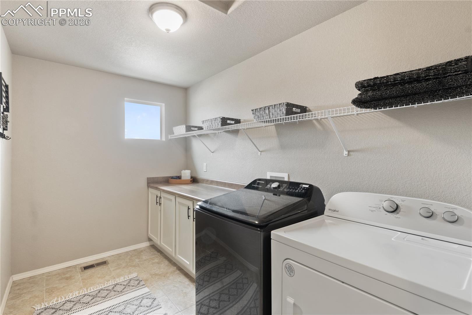 Laundry room featuring washing machine and clothes dryer, a textured ceiling, and cabinet space