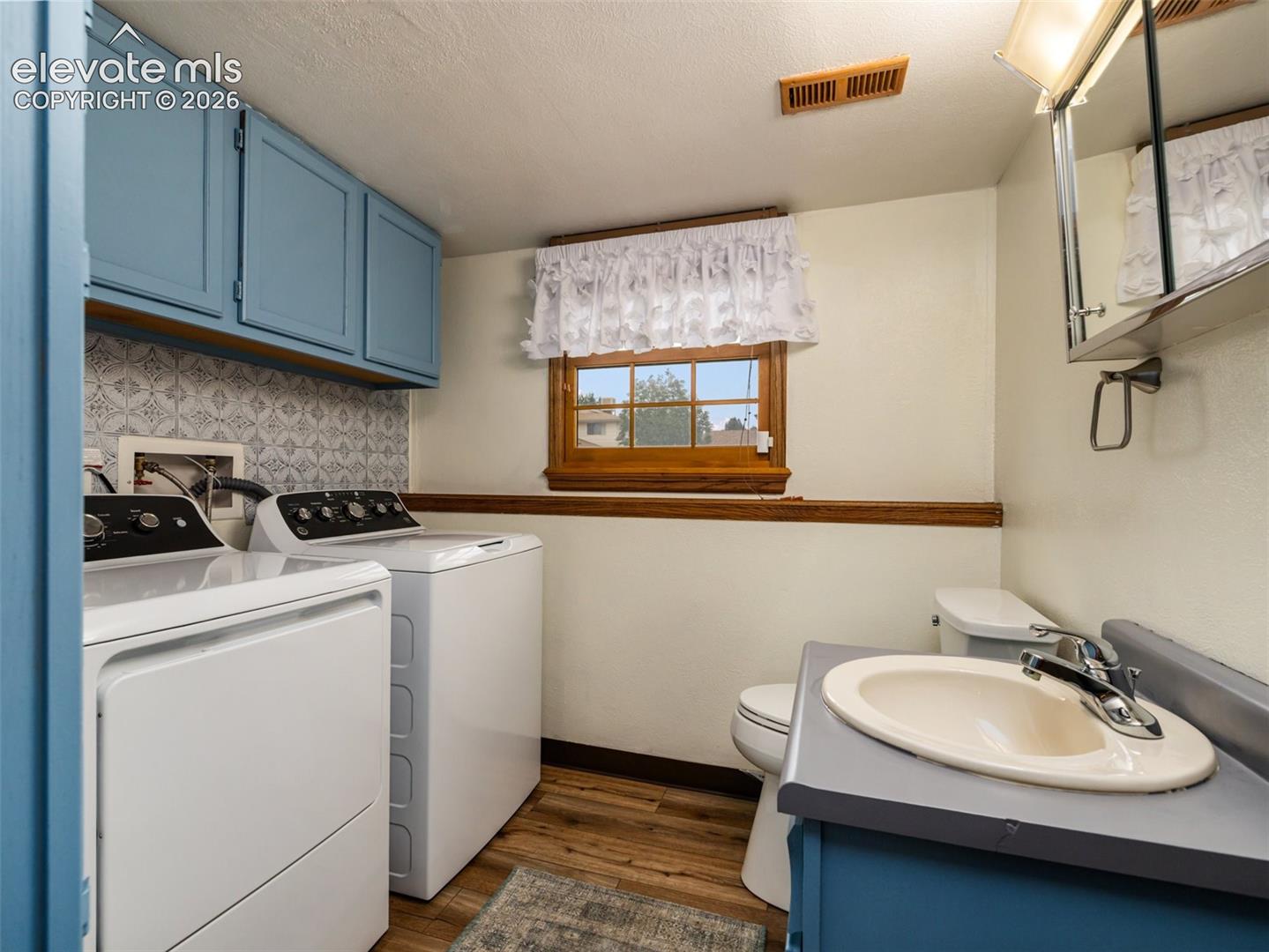 Laundry area featuring wood-finish flooring, patterned tile backsplash, and blue cabinetry