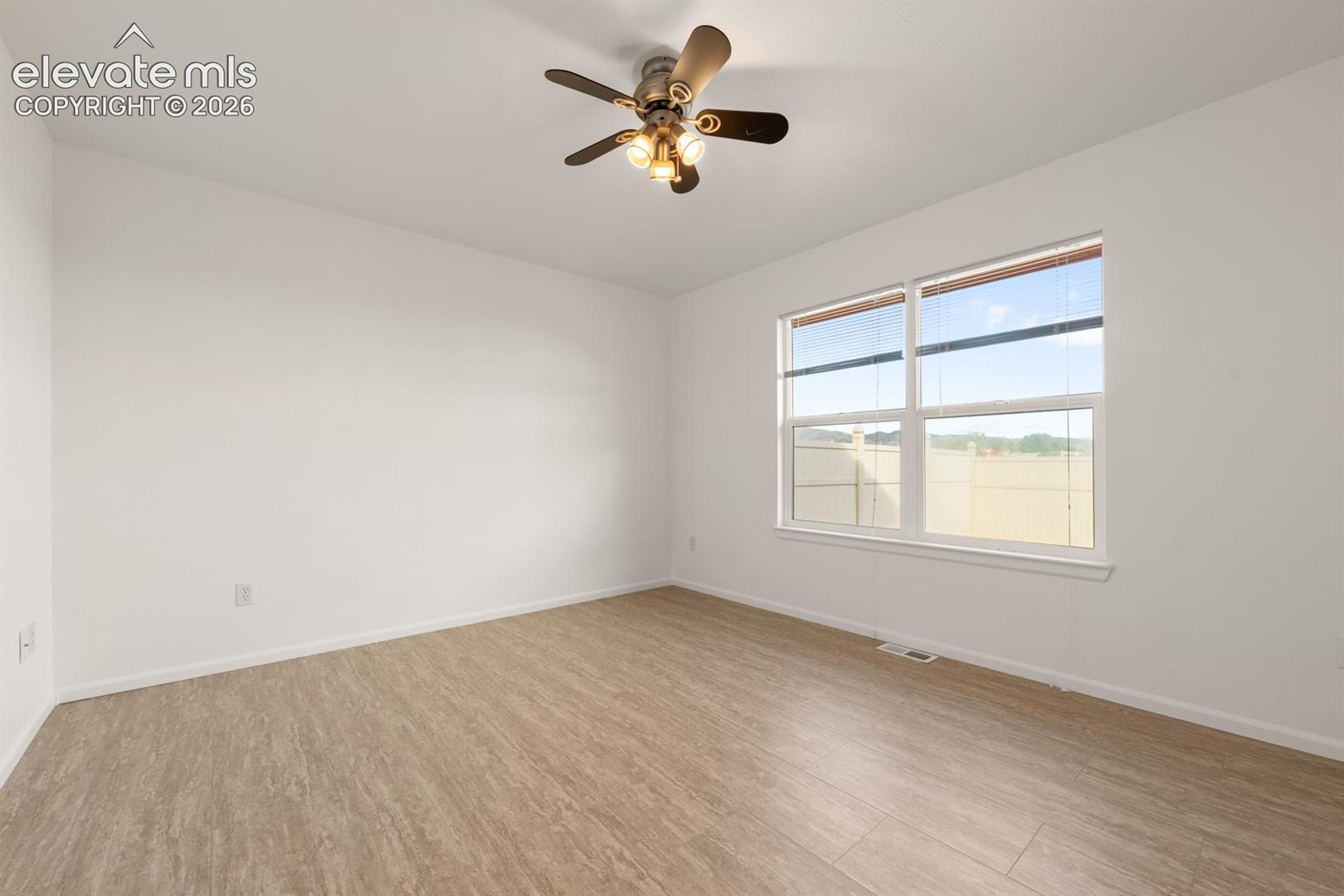 Room featuring wood-finish flooring, a multi-blade ceiling fan with integrated lighting, and a double-pane window