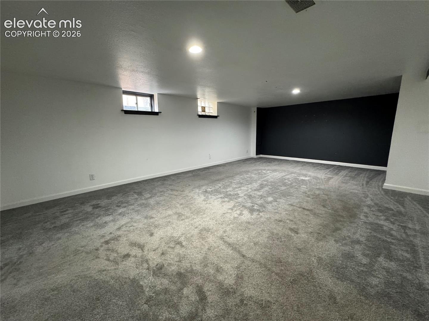 Spacious interior featuring neutral carpeting, recessed ceiling lighting, two high-set windows, and a dark accent wall