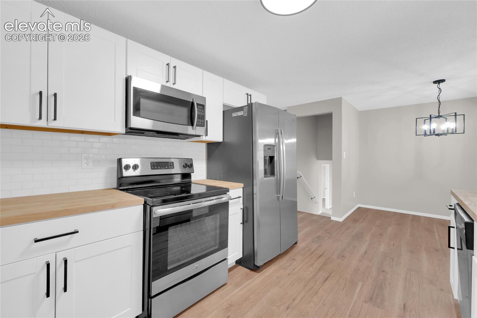 Kitchen featuring white cabinetry, wood-finish countertops, stainless steel appliances, and a subway tile backsplash