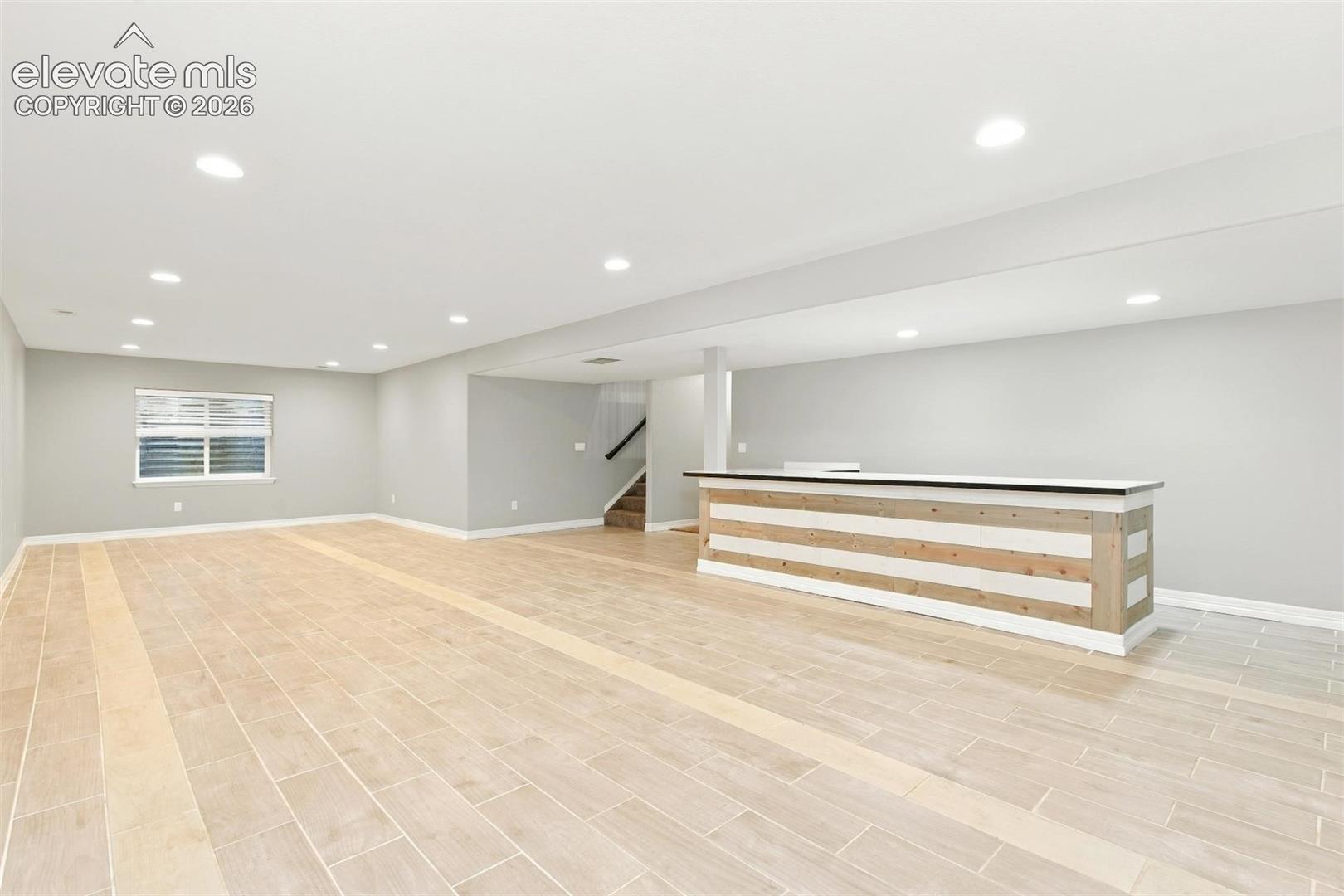 Open-concept space featuring wood-finish tile flooring, recessed lighting, and a custom built-in bar with horizontal wood-panel detailing