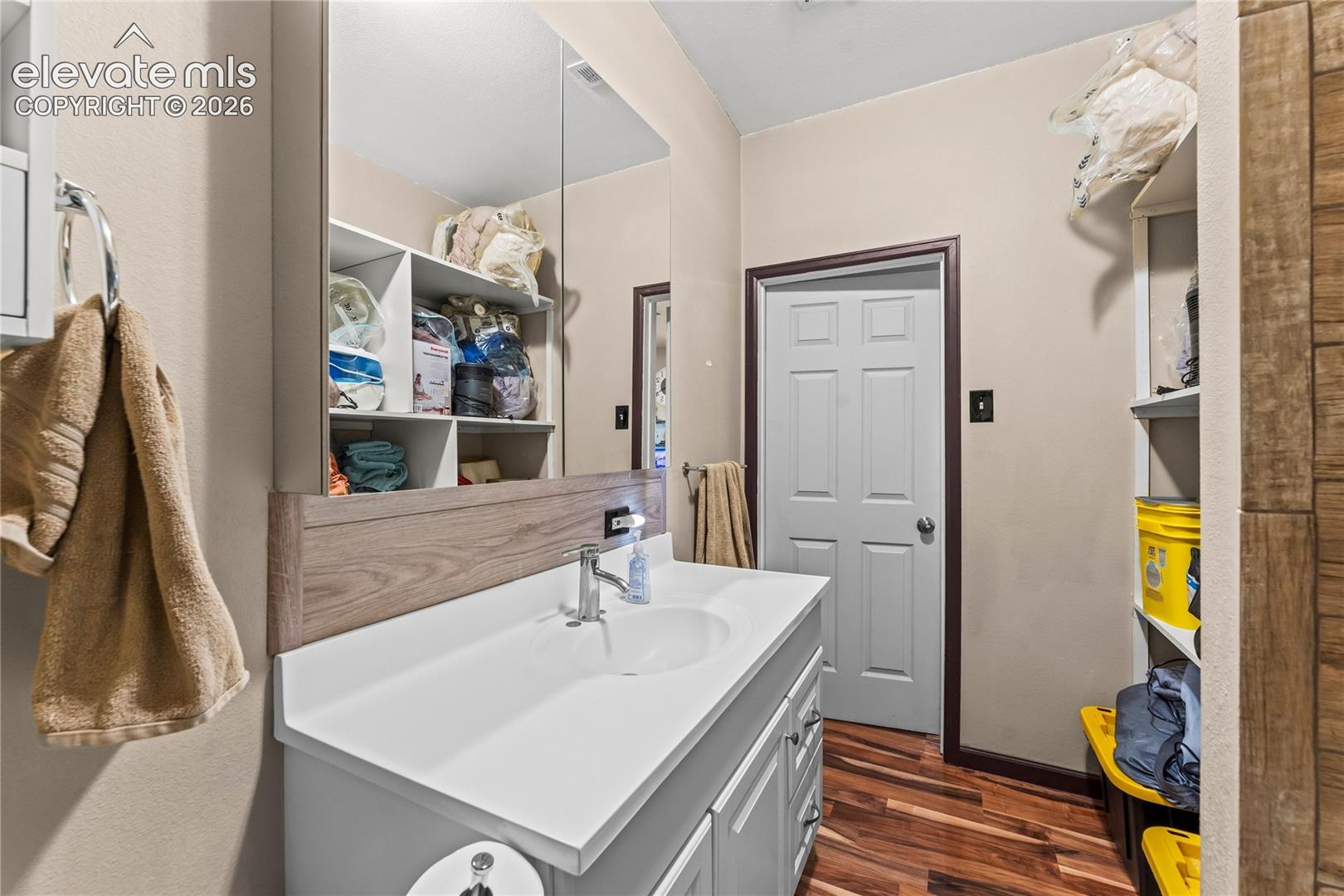 Vanity featuring a white countertop with an integrated sink, chrome faucet, wood-finish backsplash, and built-in shelving with an expansive mirror