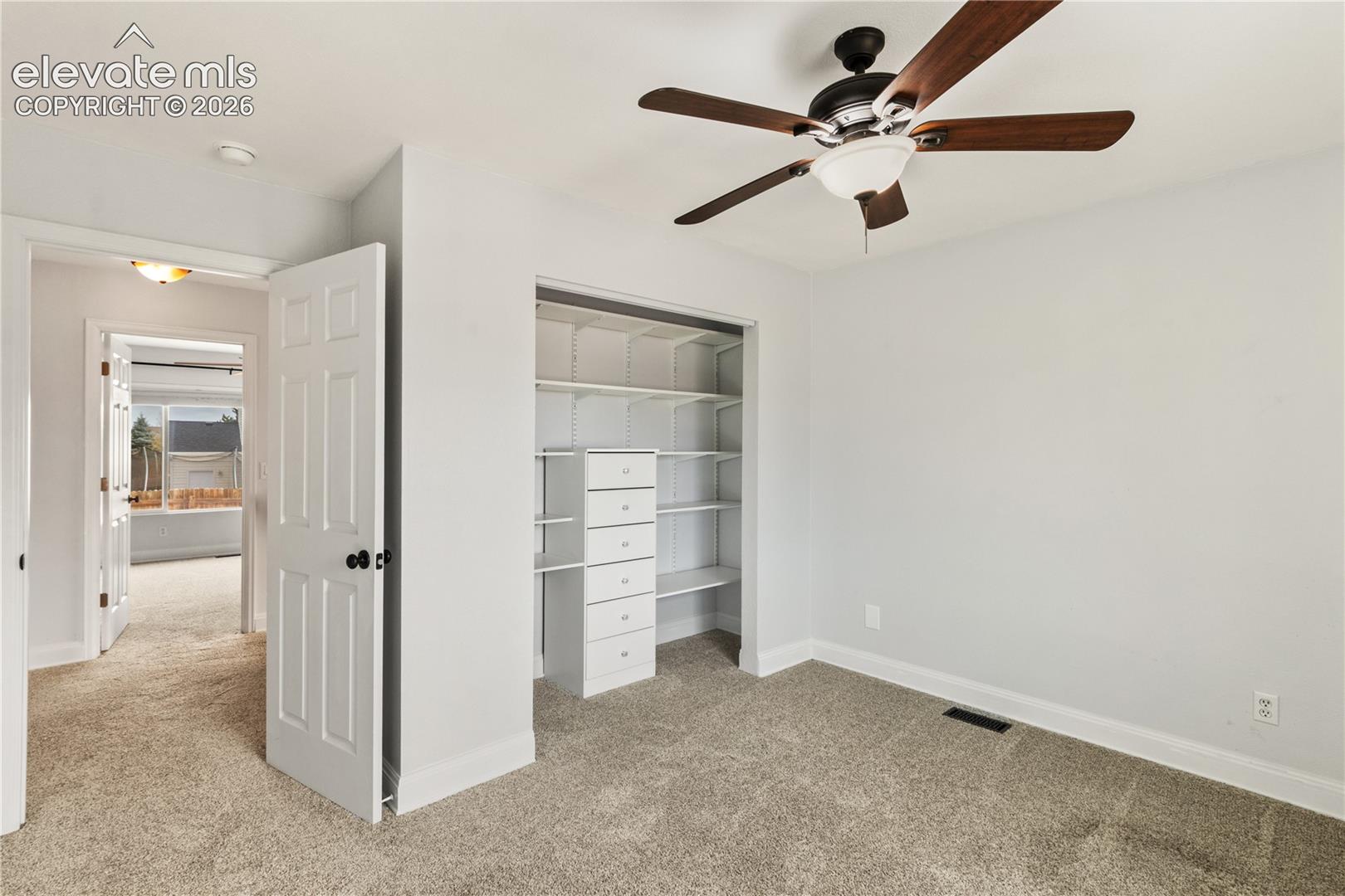 Room interior featuring neutral carpeting, a ceiling fan with integrated lighting, and a reach-in closet equipped with built-in shelving and drawer units