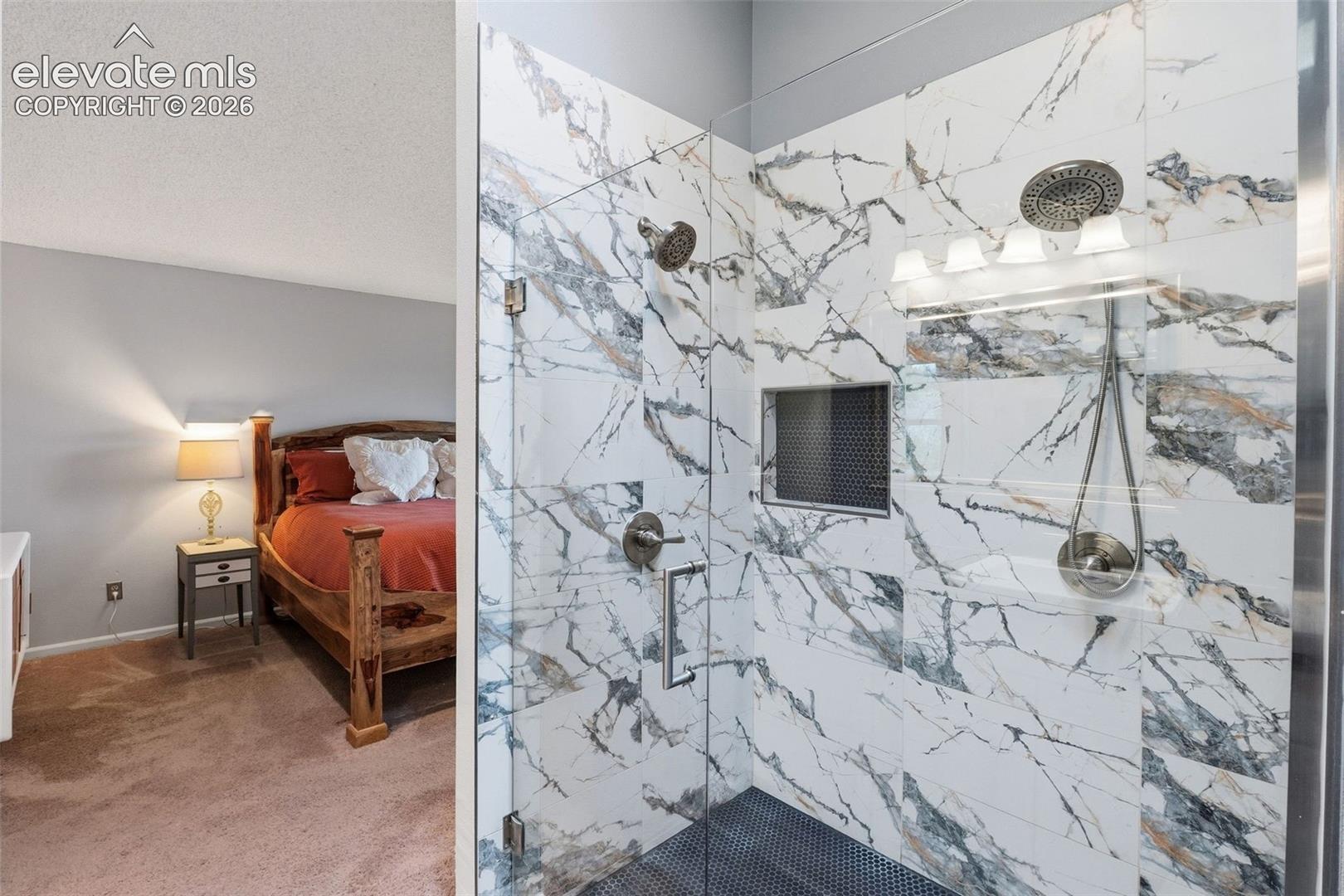 Walk-in shower with full-height marble-patterned tile, glass enclosure, recessed niche, and dual shower heads
