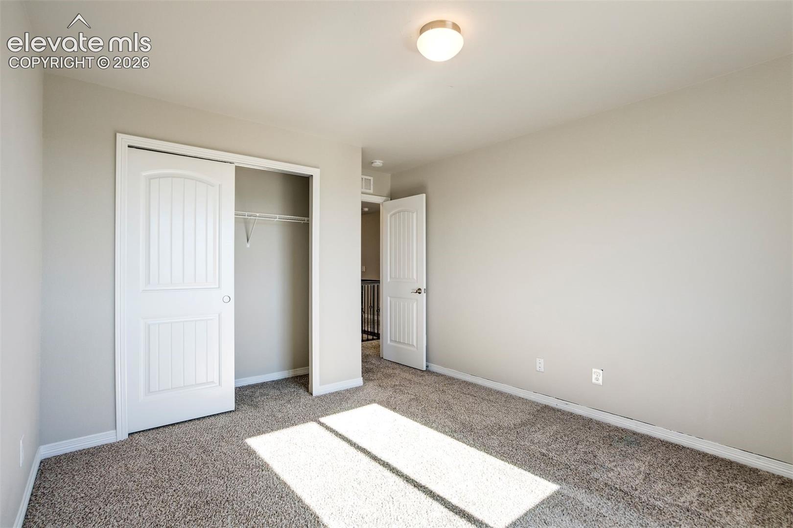 Light gray painted walls with textured carpeting, white sliding closet doors, and a flush mount ceiling light fixture