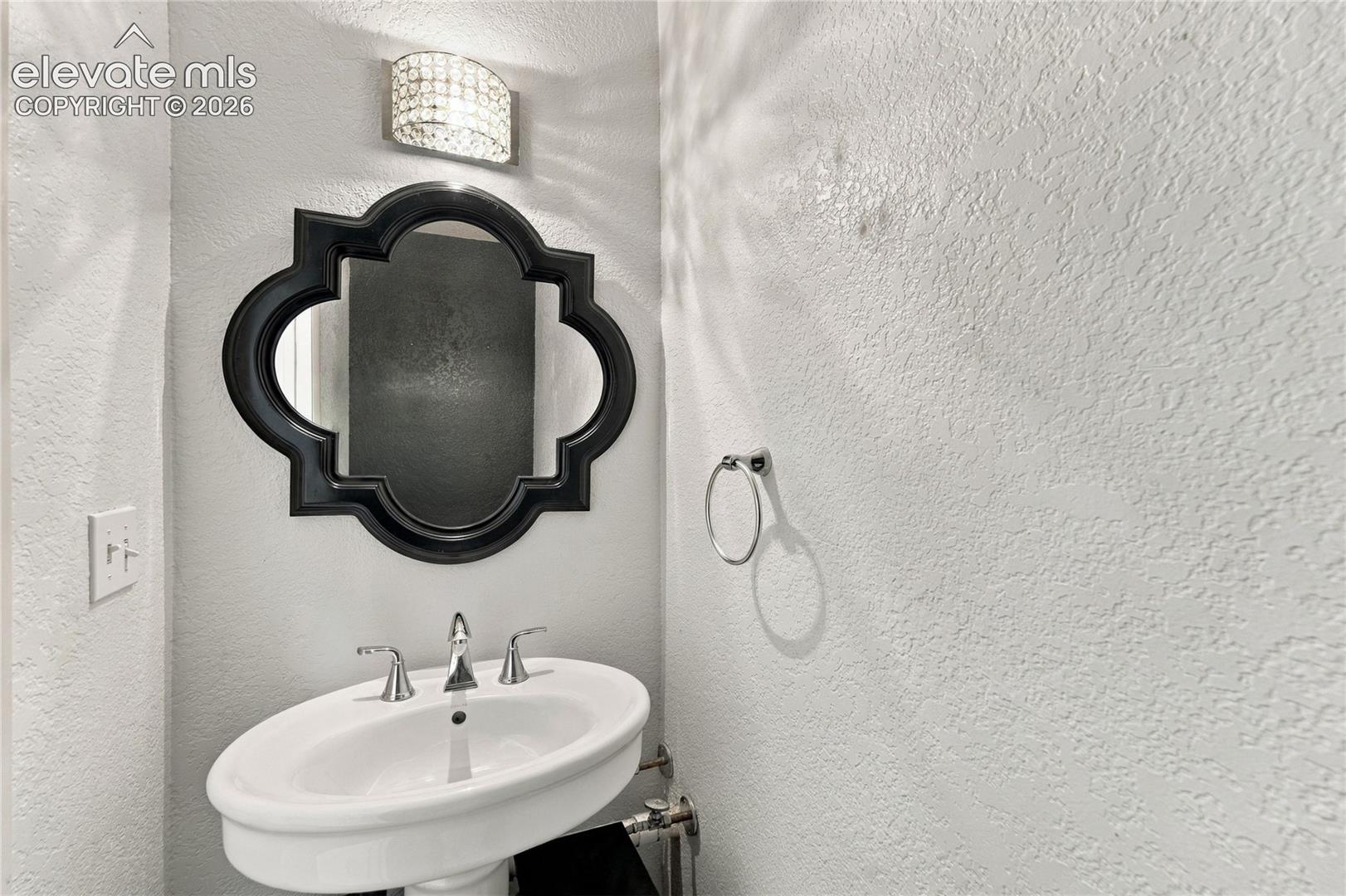 Pedestal sink with chrome widespread faucet, decorative quatrefoil-framed wall mirror, and modern crystal-style sconce