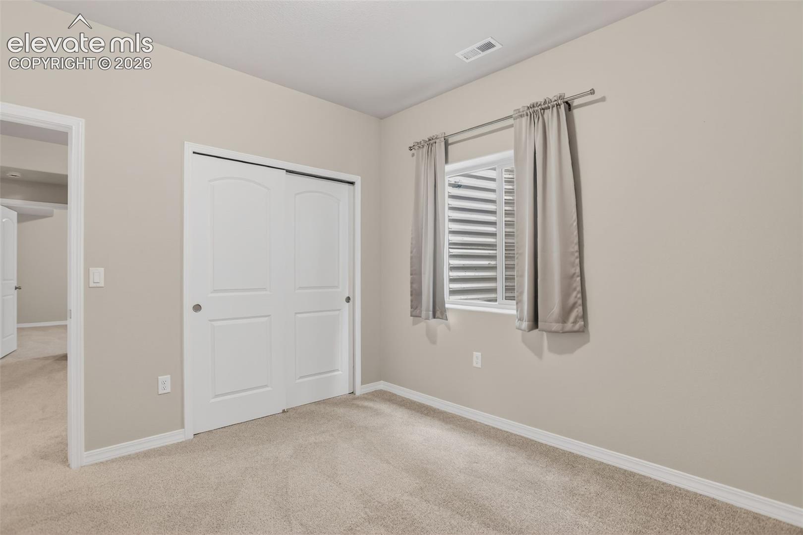 Carpeted room featuring light beige walls, a built-in closet with white bi-fold doors, a single window with horizontal blinds, and white trim