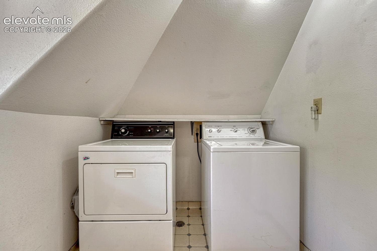 Built-in laundry appliances with a tiled floor and overhead shelving