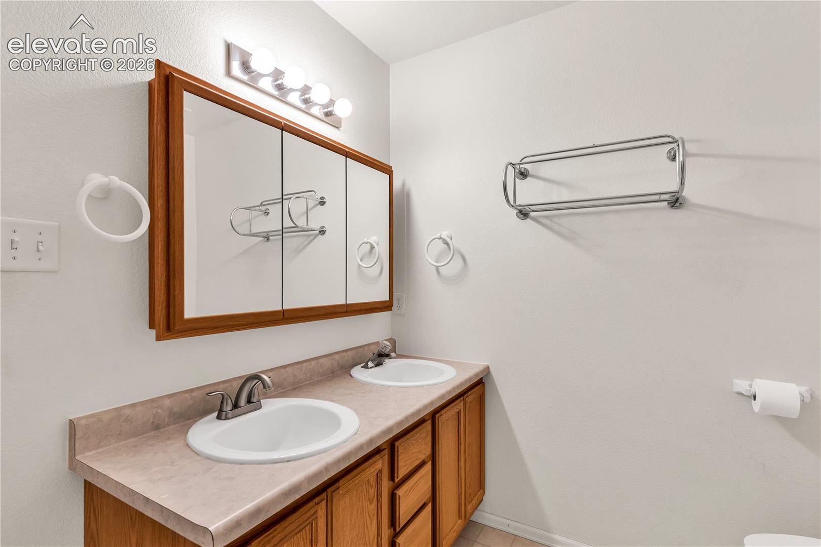 Double vanity with wood-finish cabinetry and integrated sinks, complemented by a triple mirrored medicine cabinet and overhead lighting