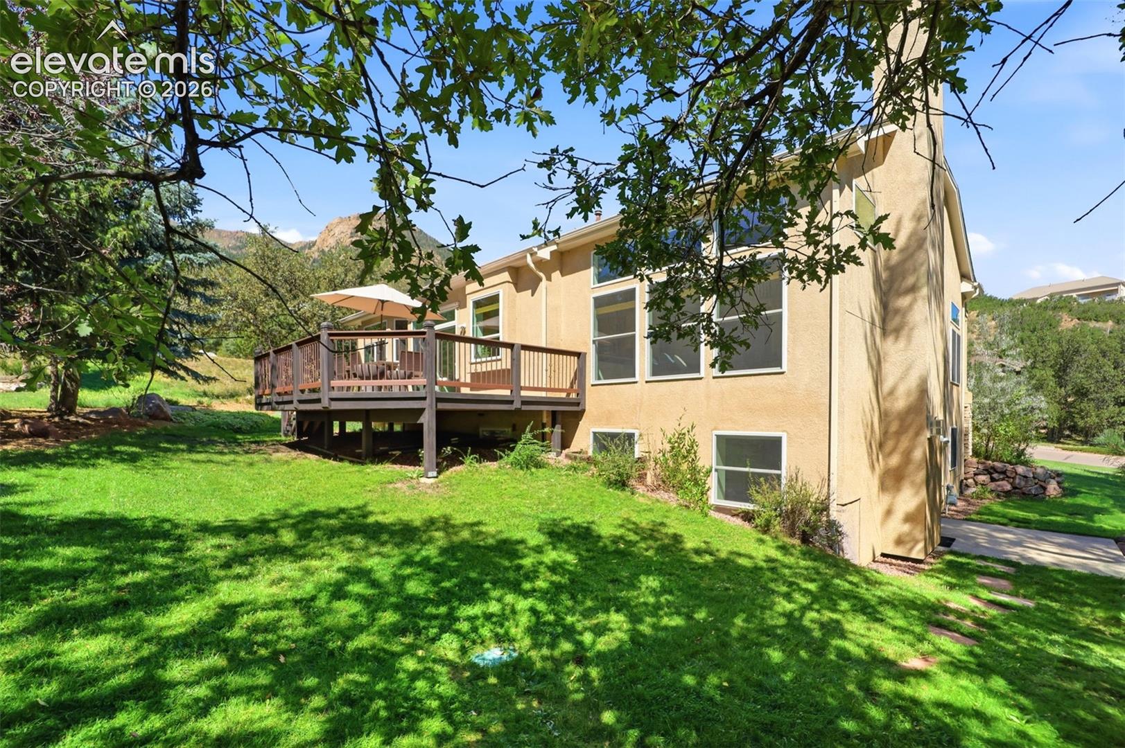 Expansive rear deck, stucco exterior, multiple large windows, and a generous green lawn