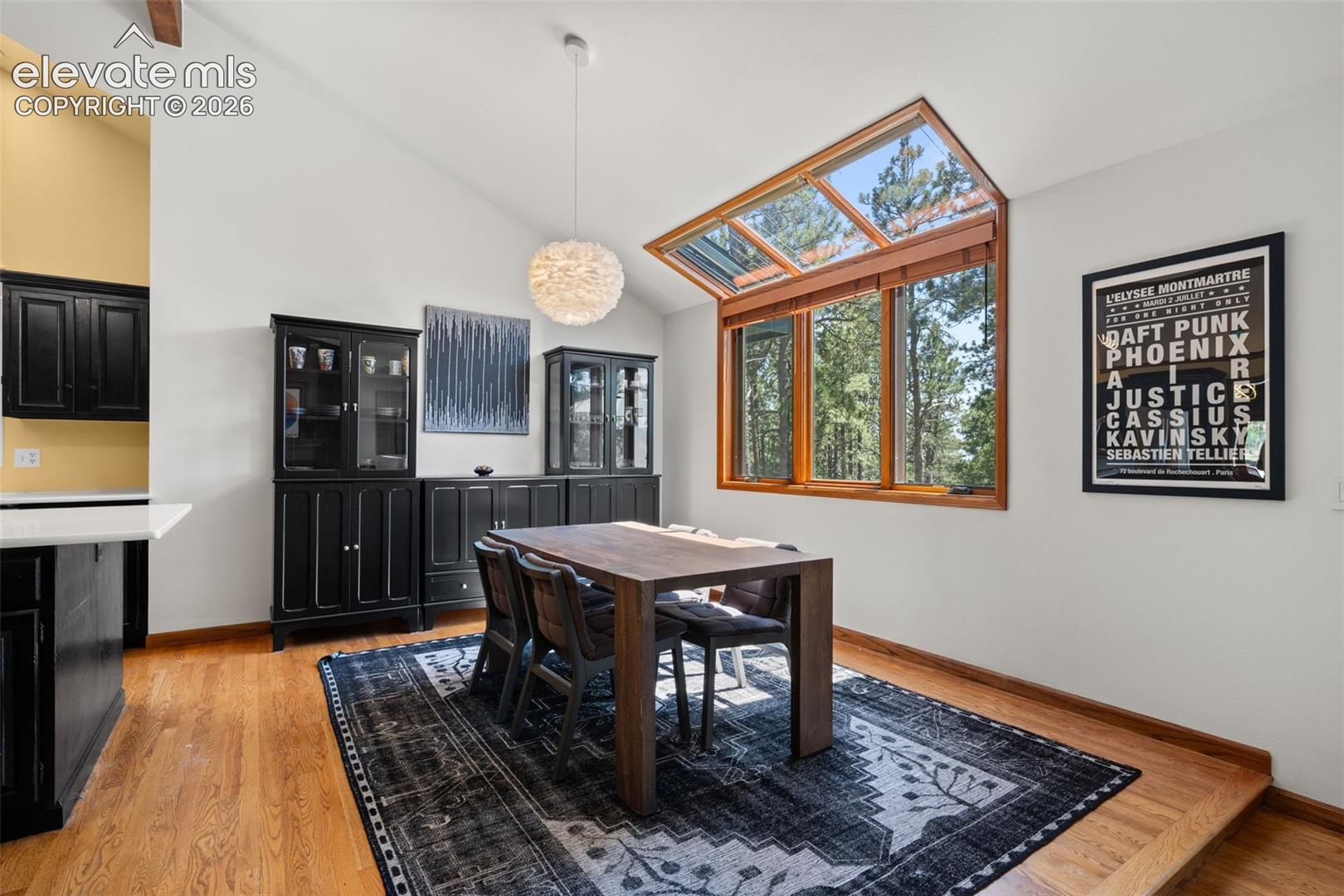 Vaulted ceiling dining area featuring wood-finish flooring and extensive window coverage