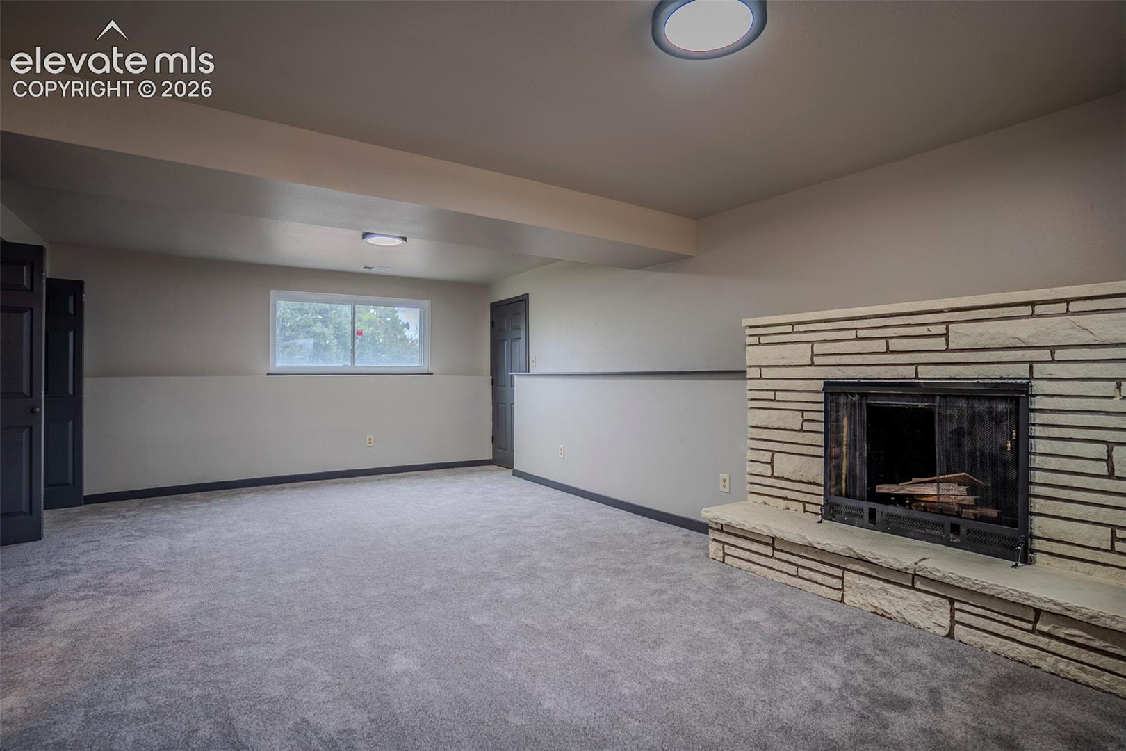 Interior room featuring a fireplace with a textured stone surround and stone hearth, wall-to-wall carpeting, and flush-mount lighting fixtures