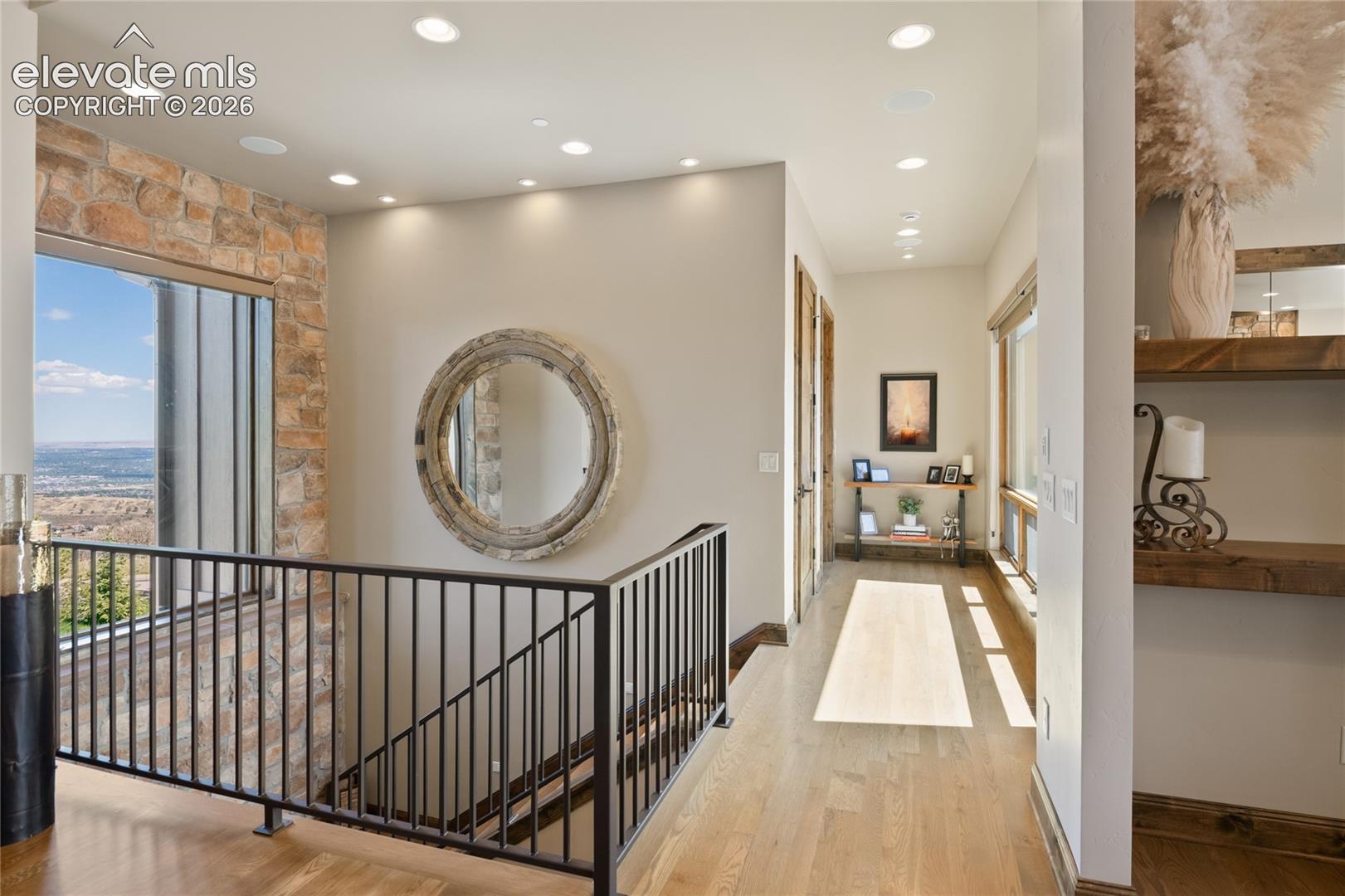 Light-filled upper hallway with white oak flooring, custom iron railing, floating shelves, and expansive windows overlooking Colorado Springs.