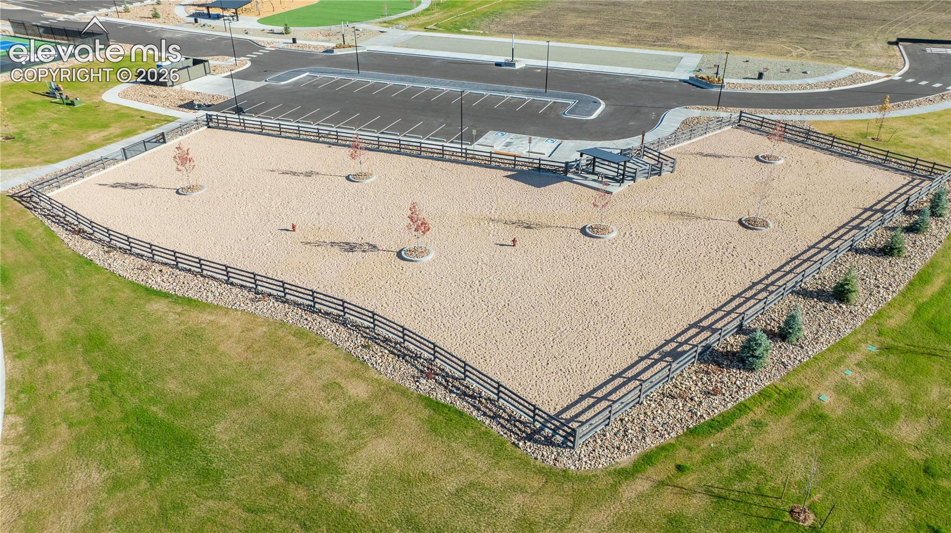 Fenced enclosure featuring a gravel surface, perimeter post-and-rail fencing, and young specimen trees