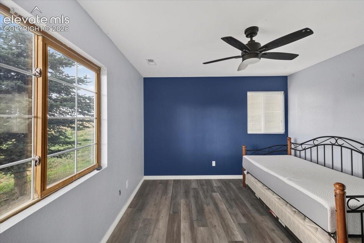 Room featuring vinyl wood-finish flooring, a large multi-pane window with wood trim, and a ceiling fan with integrated lighting
