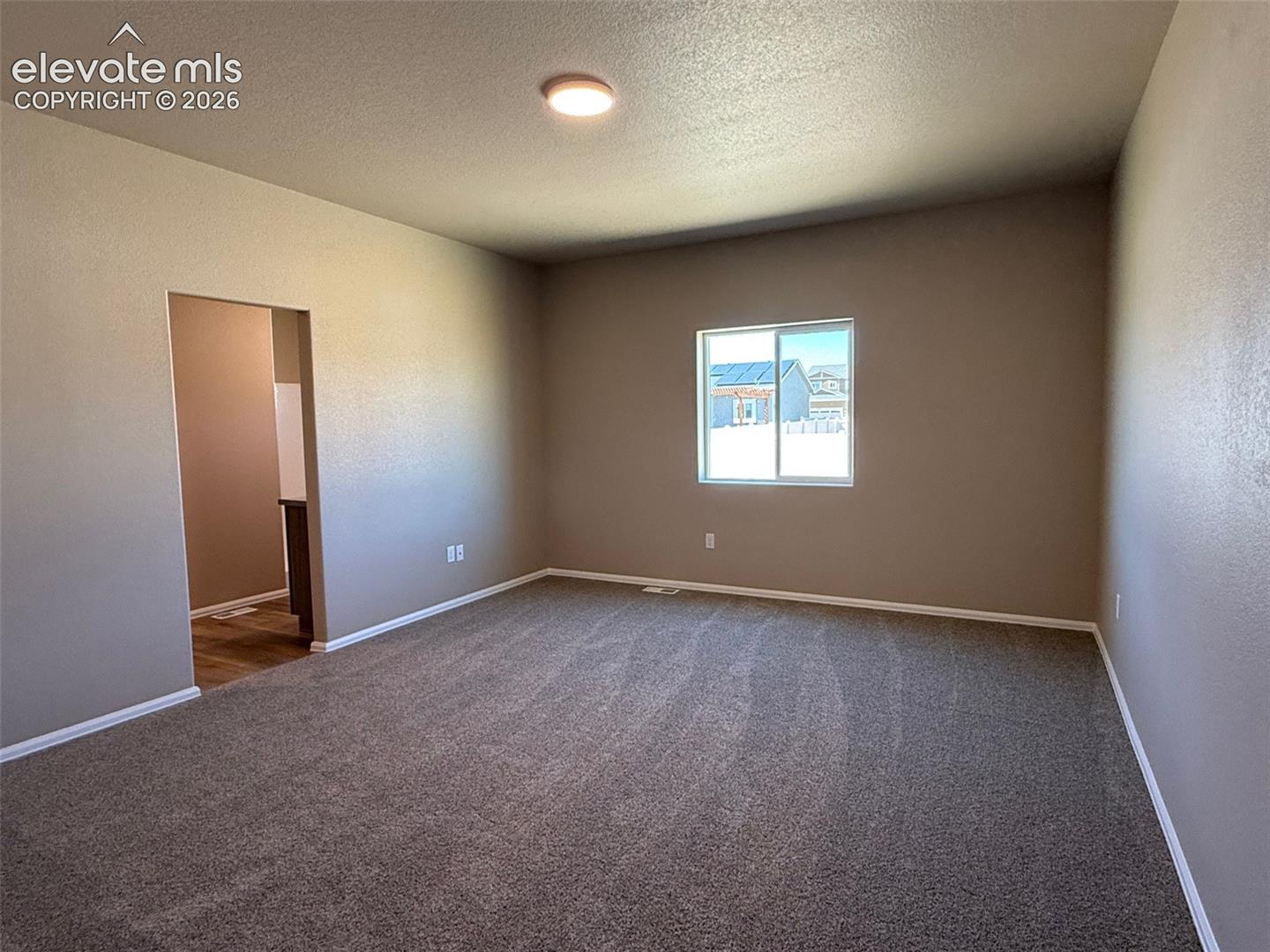 Spacious room featuring carpeting, neutral wall tones, a recessed window, a flush mount ceiling light, and an open doorway