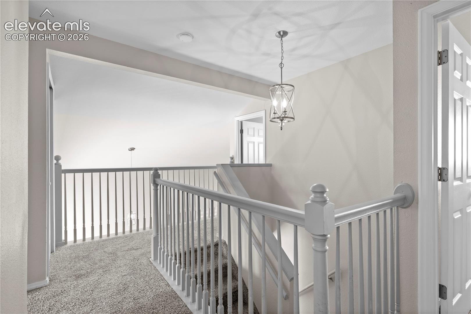 Landing area featuring neutral carpeting, a decorative metal lantern-style pendant light, and a painted wood railing with spindle balusters