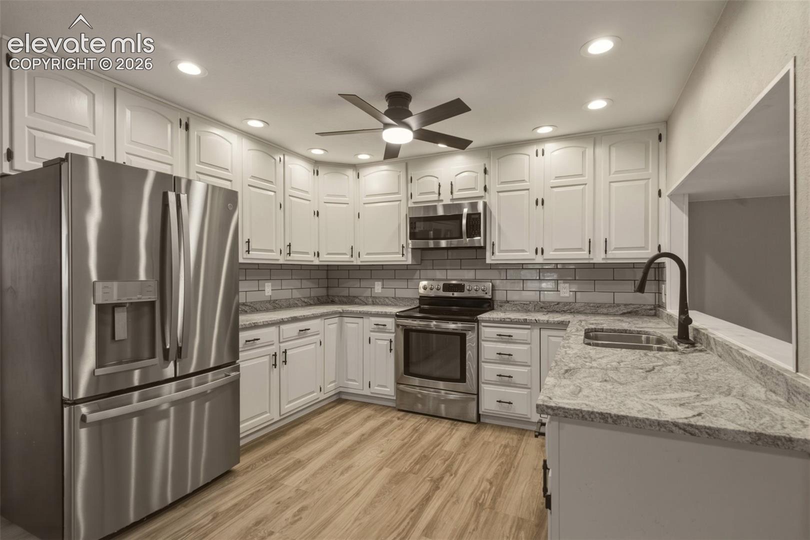 White cabinetry with dark hardware, stainless steel appliances, light wood-finish flooring, recessed lighting, and a pass-through window