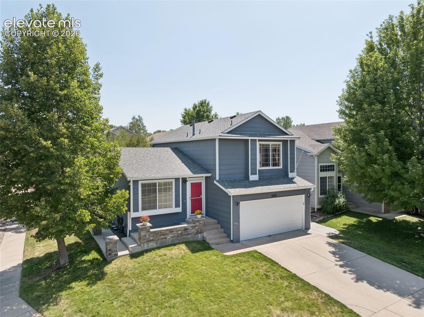 Two-story residence featuring a gray exterior, attached garage, and a red entry door