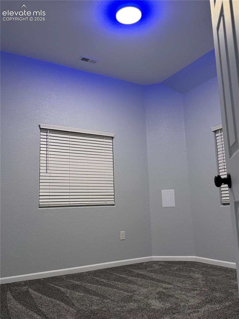 Recessed ceiling light with accent lighting, window with horizontal blinds, gray textured walls, gray patterned carpeting, and white trim