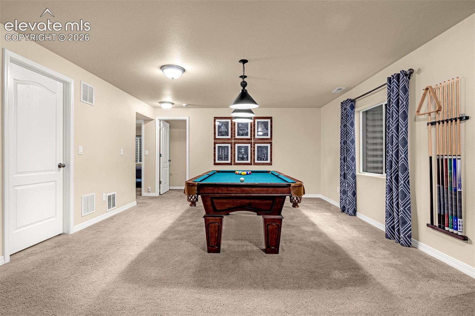 Spacious room featuring neutral carpeting, recessed ceiling lighting, a multi-tier pendant fixture, and arched-panel interior doors