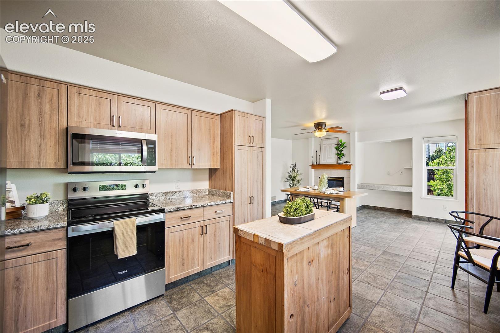 Kitchen featuring wood-finish cabinetry, stainless steel appliances, granite countertops, and tile flooring