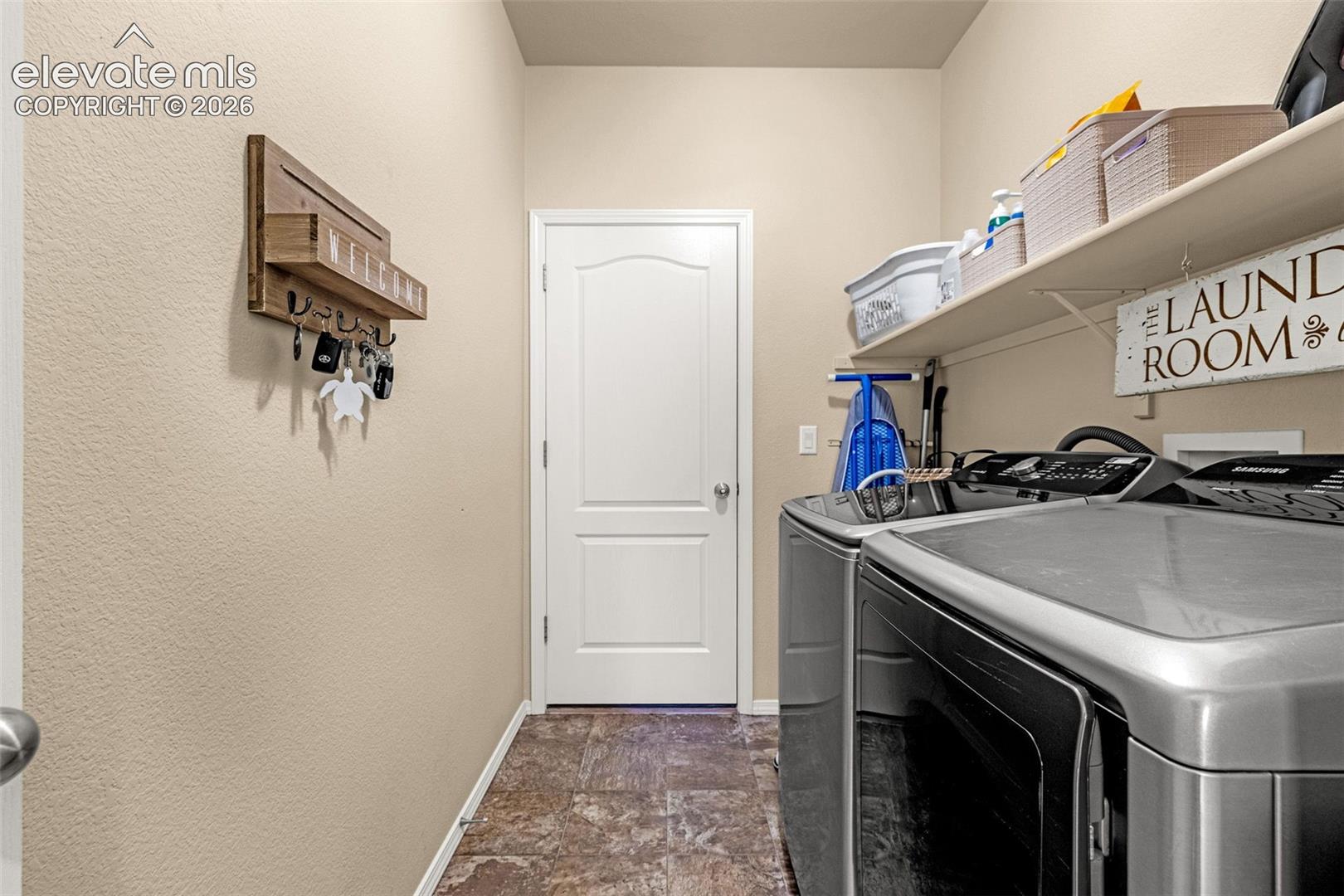 Multi-purpose utility space featuring stone-style flooring, a solid core interior door, and built-in shelving