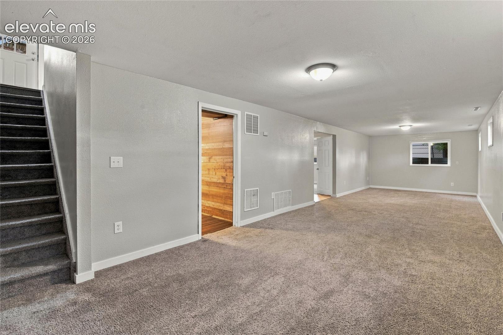 Huge basement area with carpeted flooring throughout, recessed window, white trim, and staircase that goes into the kitchen/dining area