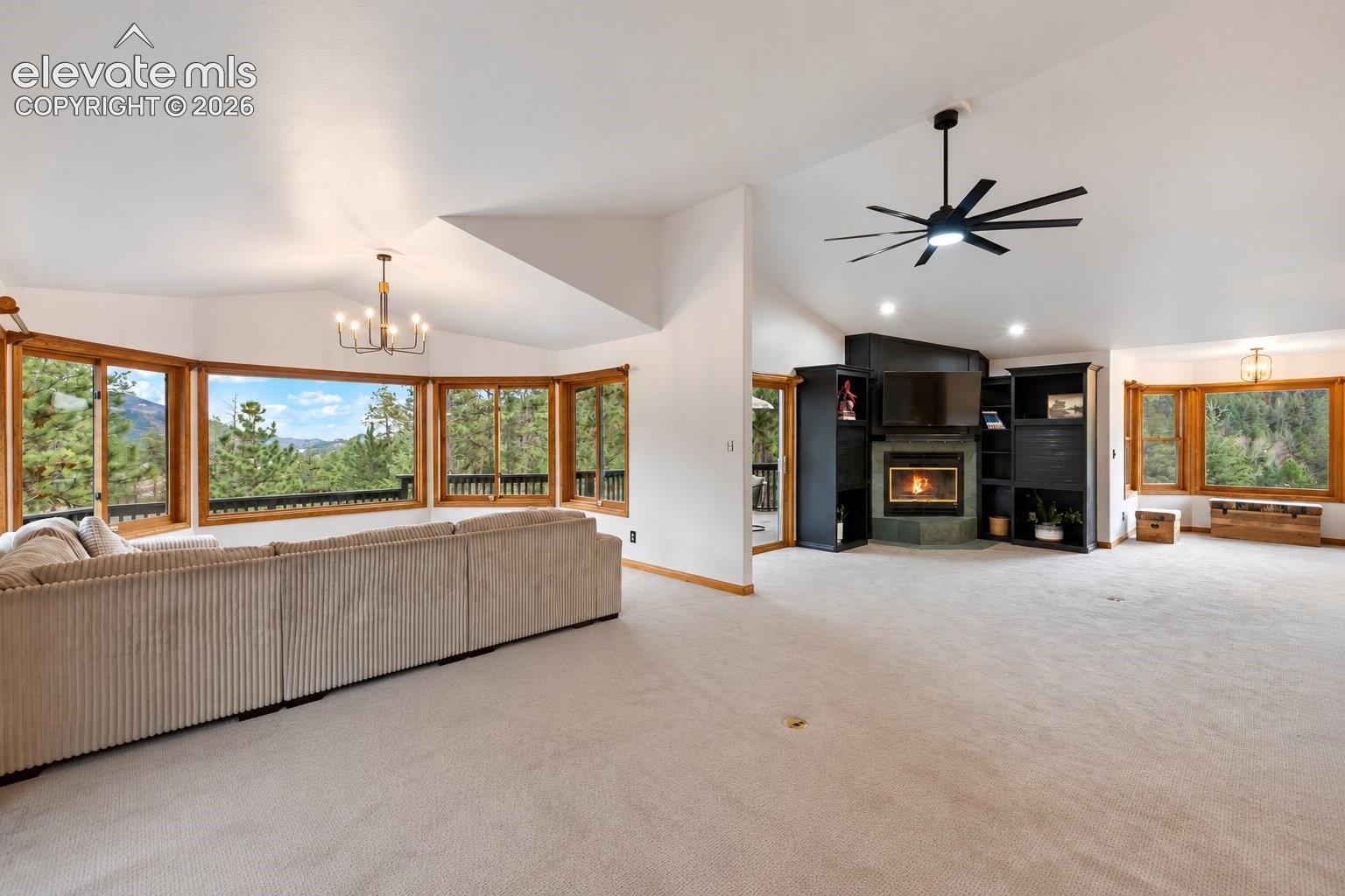 Vaulted ceilings, expansive bay windows, fireplace with built-in shelving, multi-blade ceiling fan, and multi-light chandelier