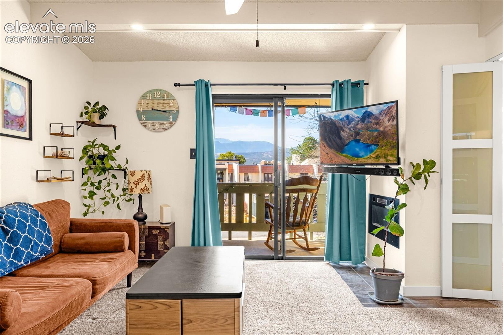 Sliding glass door leading to a balcony, ceiling-mounted light fixtures, built-in wall shelving, and a wall-mounted television