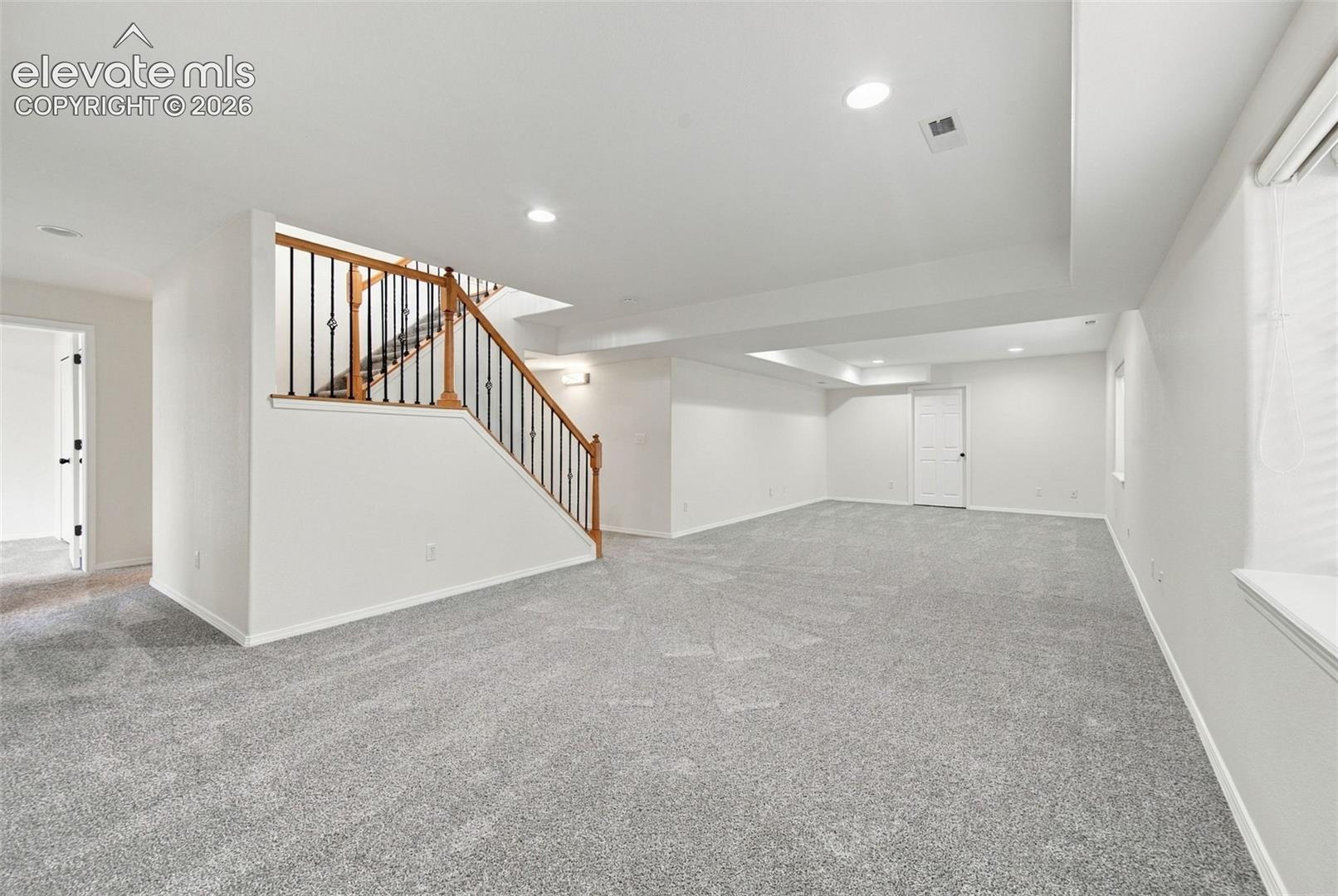 Open-concept interior featuring neutral carpeting, recessed lighting, and a staircase with wood handrails and black metal balusters