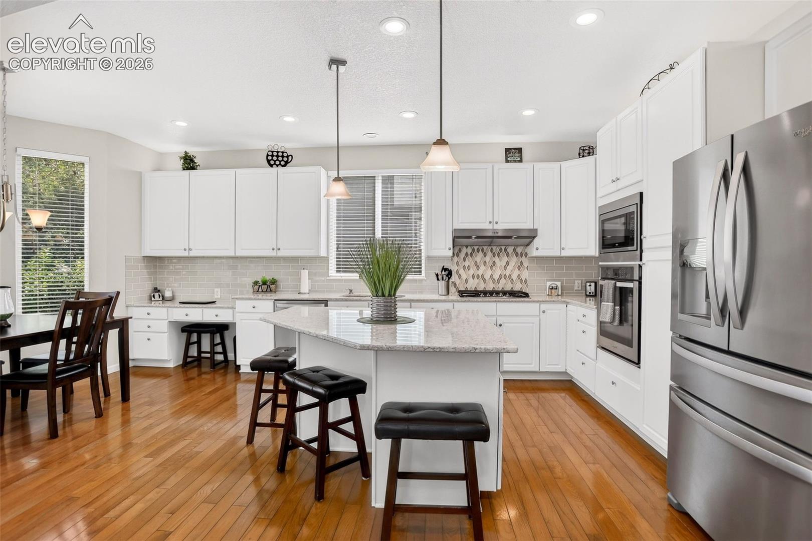 Kitchen featuring wood-finish flooring, white cabinetry, a built-in oven, stainless steel refrigerator, and a kitchen island with seating