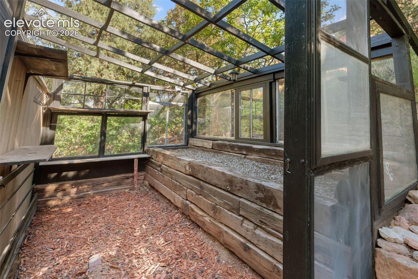 Enclosed greenhouse structure featuring a slatted roof, multiple window panels, and a built-in wooden planting bed