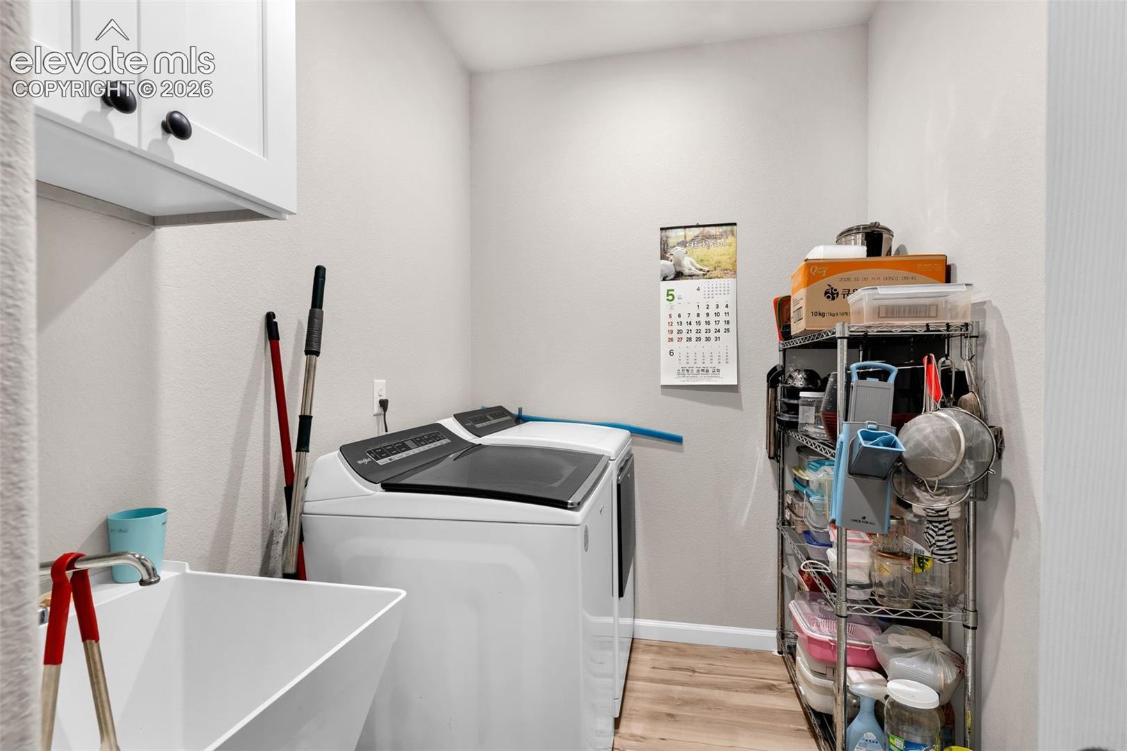 Dedicated laundry area featuring a utility sink, upper cabinetry with black hardware, and wood-finish flooring