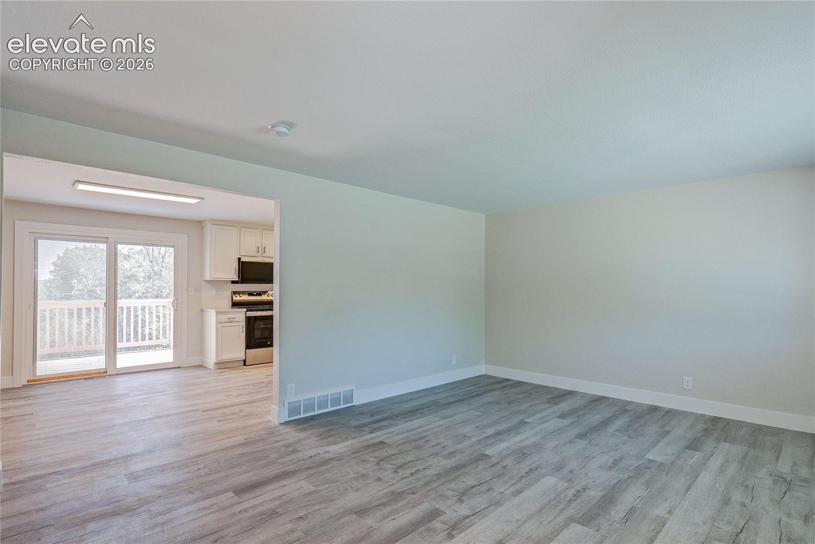 Open-concept interior featuring light wood-finish flooring, neutral wall paint, and sliding glass doors with exterior balcony access
