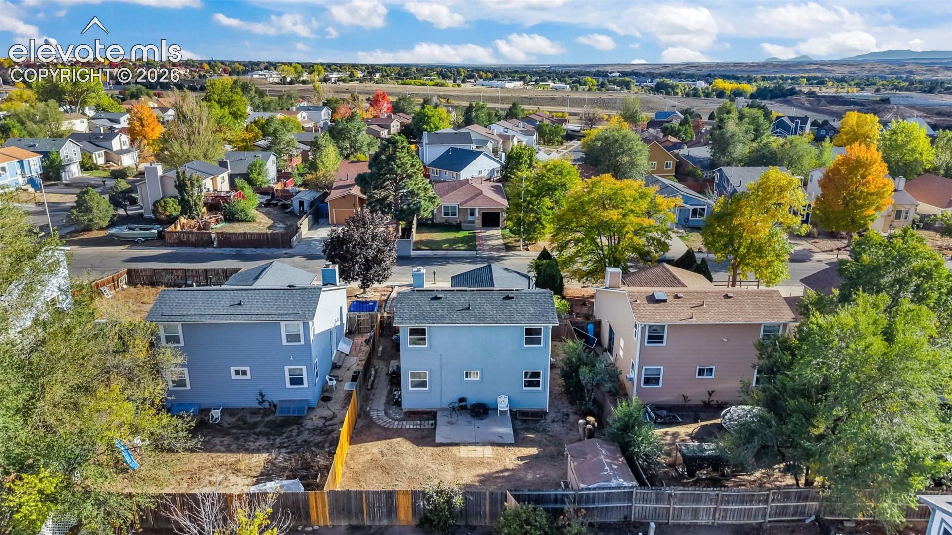 Aerial perspective of suburban properties featuring asphalt shingle roofing, paved rear patios, and fenced yards