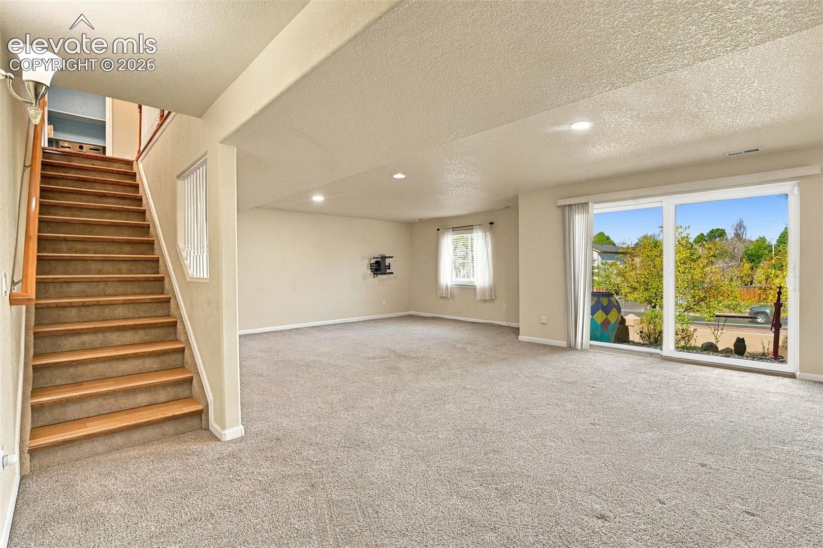 Open-concept interior featuring carpeted flooring, a staircase with wood-finish treads, recessed lighting, and expansive floor-to-ceiling glass sliding doors