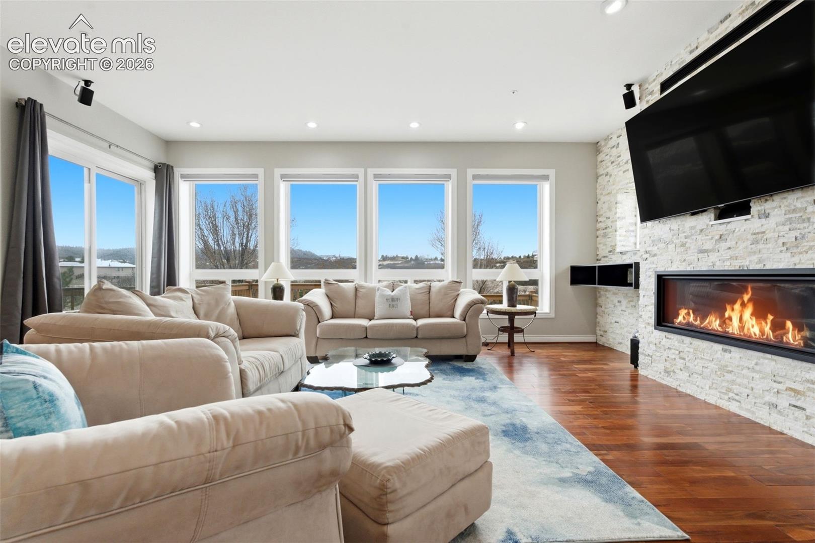 Hardwood flooring, recessed lighting, and a linear fireplace with a stone-clad surround