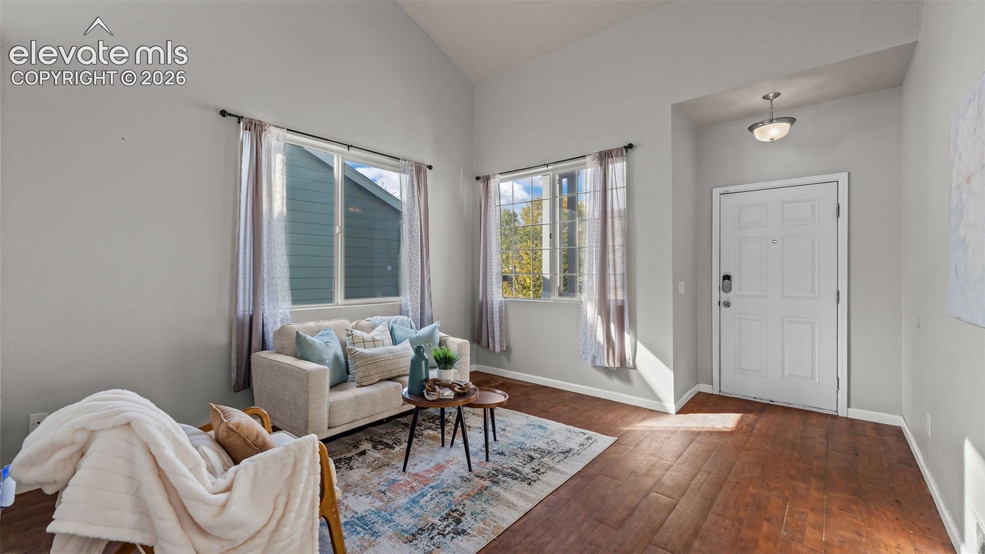 Vaulted ceiling, wood-finish flooring, white paneled entry door, and a flush mount light fixture
