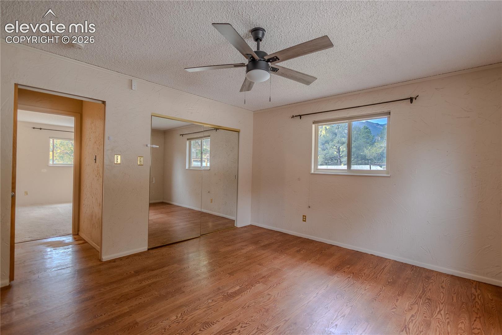 Room featuring wood-finish flooring, a ceiling fan with integrated lighting, mirrored sliding closet doors, and windows with mountain scenery