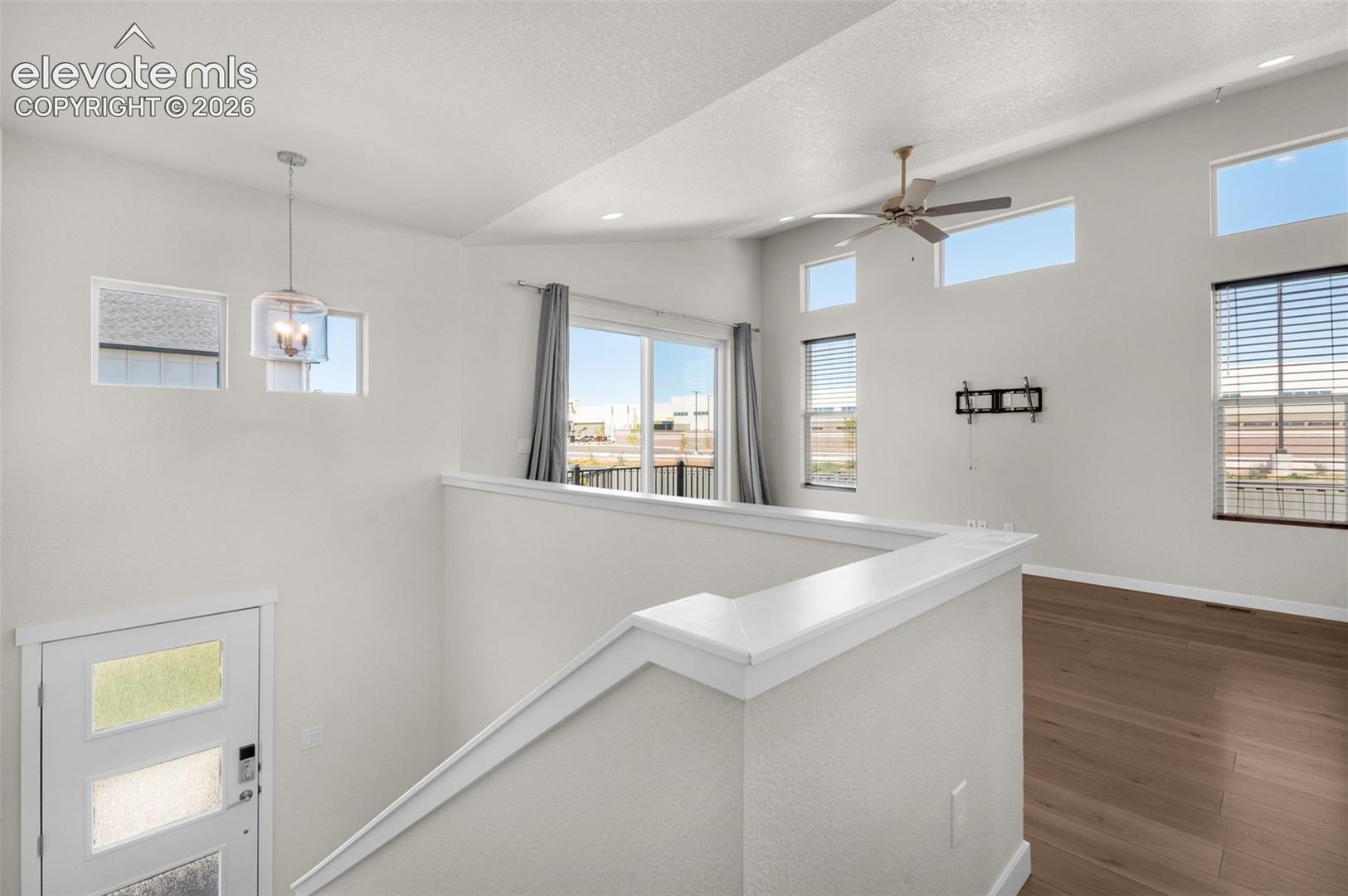 Vaulted ceilings, wood-finish flooring, multi-level windows, modern pendant lighting, and a sliding glass door