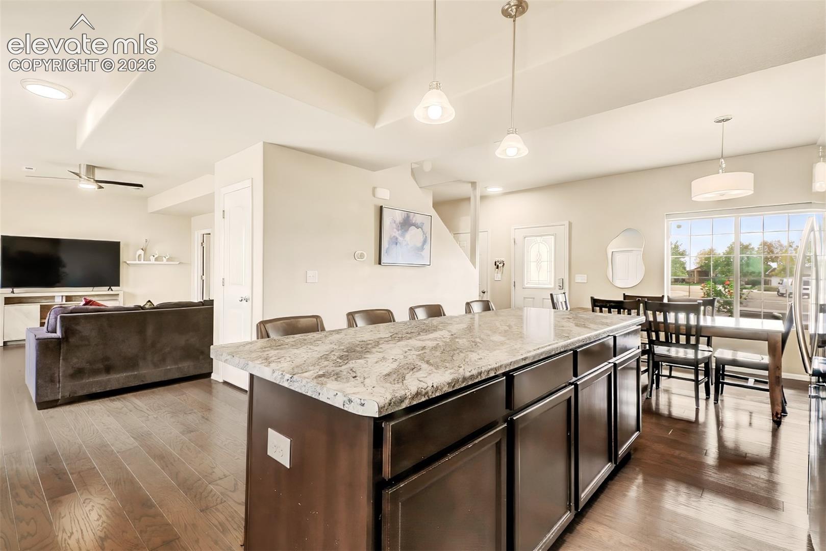 Kitchen island featuring a stone-look countertop, dark cabinetry, wood-finish flooring, recessed lighting, and pendant fixtures